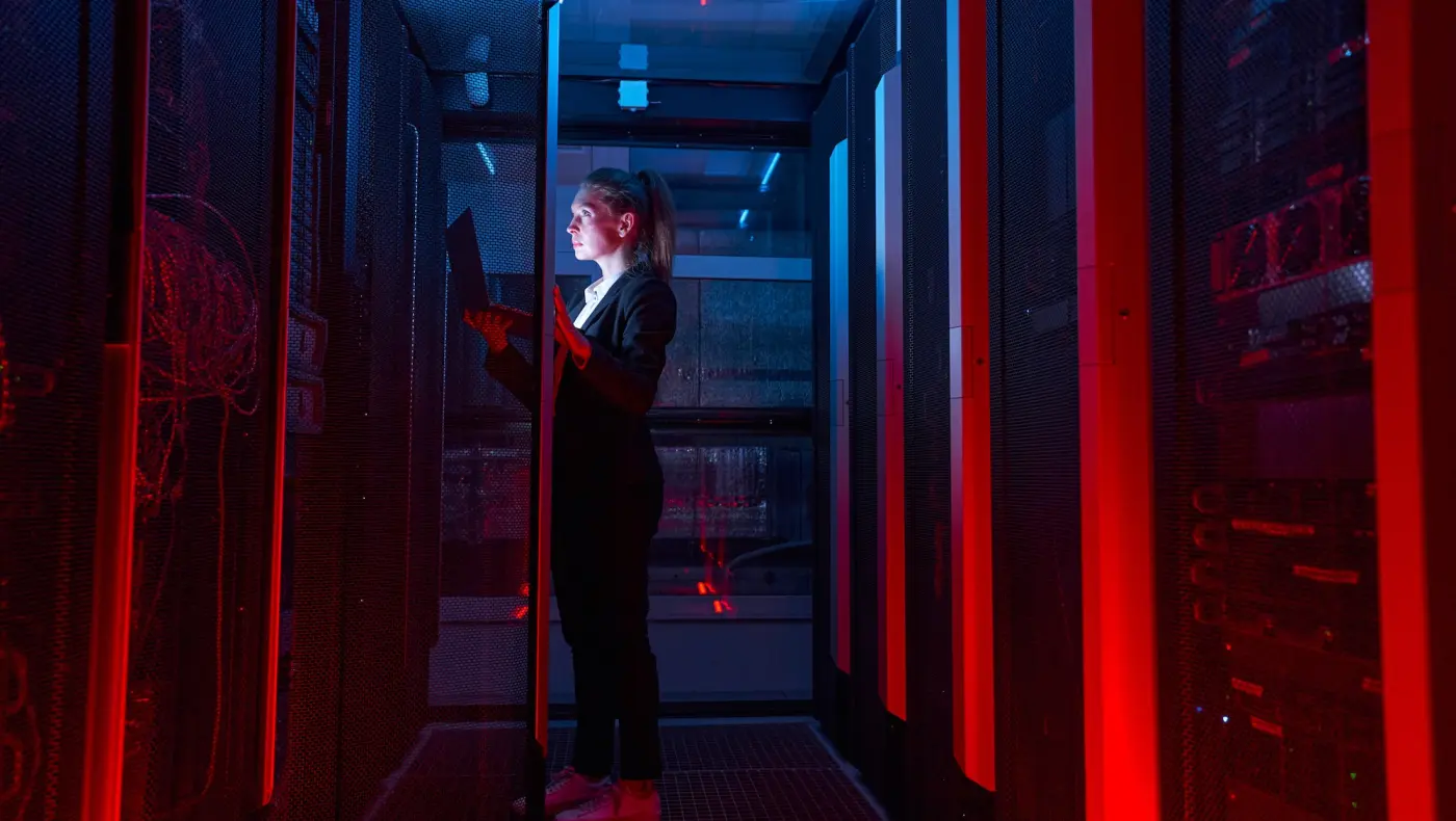 Pracovnice v serverovně ICT mezi serverovými rozvaděči při kontrole technické infrastruktury.